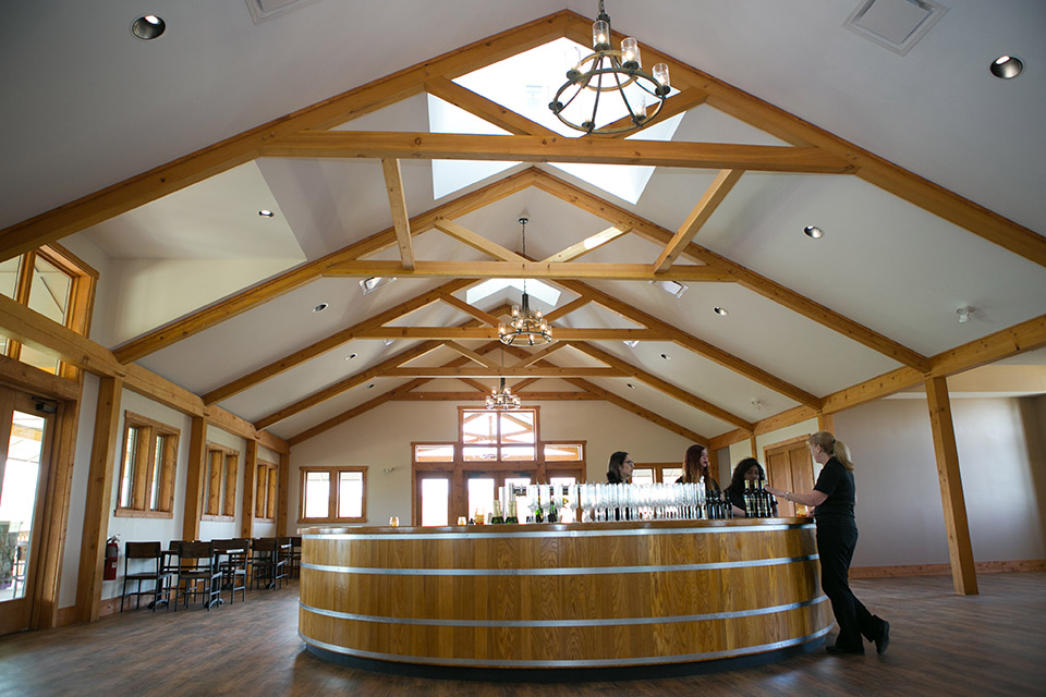 A wine tasting room in the Poconos with a vaulted ceiling and two patrons being served by a worker.