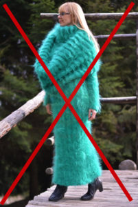 A woman in an aqua Angora sweater dress stands amongst pine trees.
