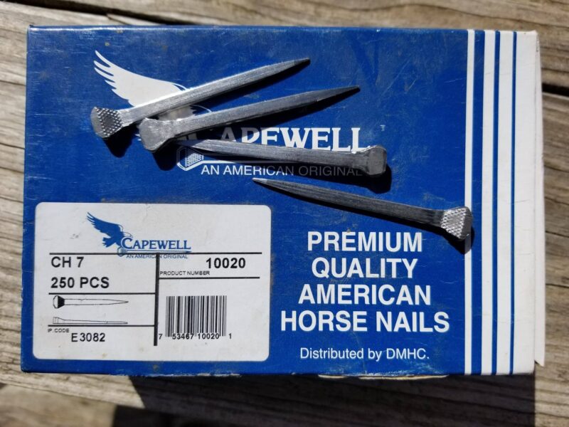A blue box of horseshoe nails with 4 horse nails on top A blue box of horseshoe nails with 4 horse nails on top
