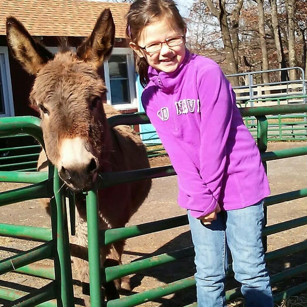 A young girl stands next to our donkey, Mandy.