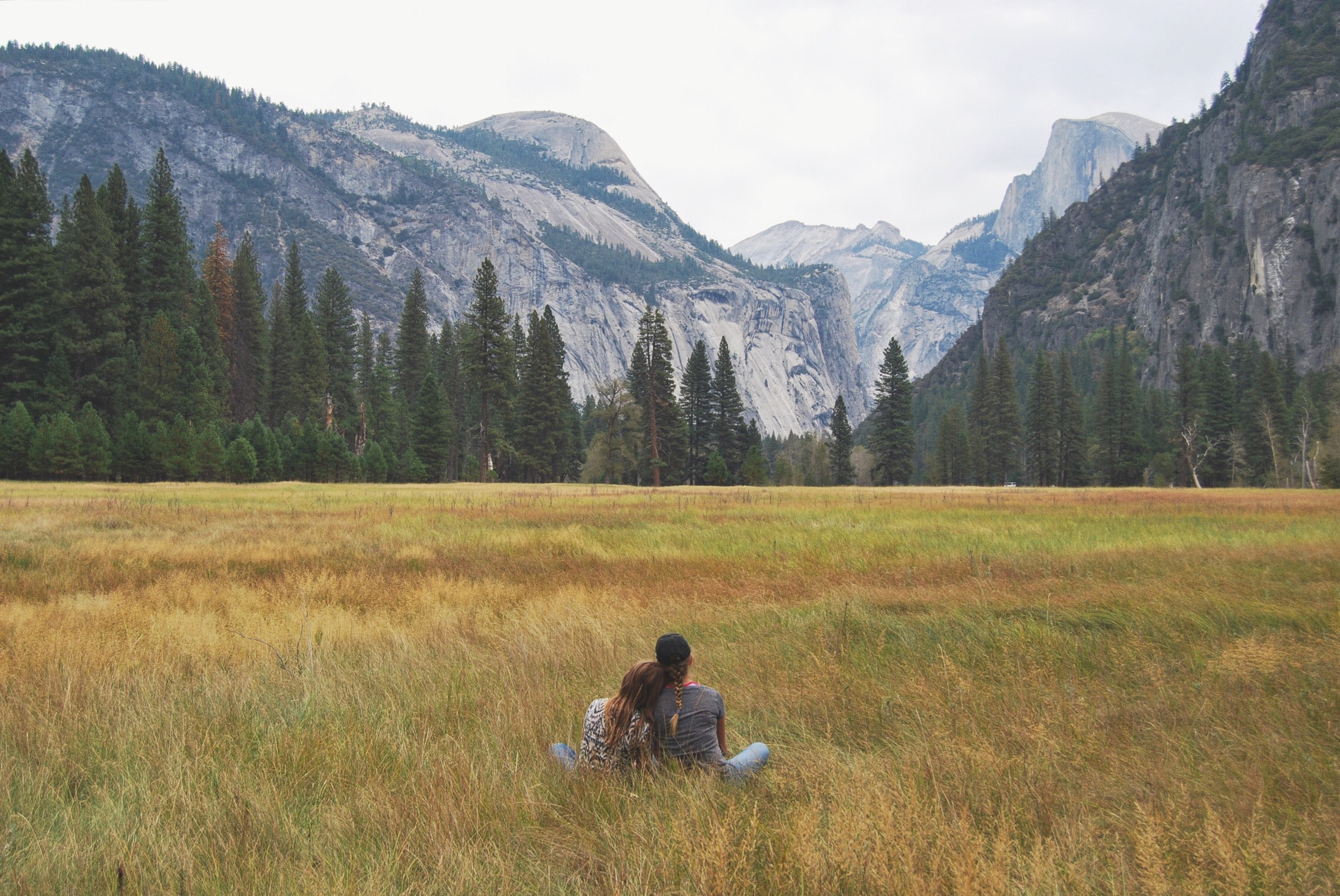 Couple Sitting in Grass Field Looking at Mountain Range