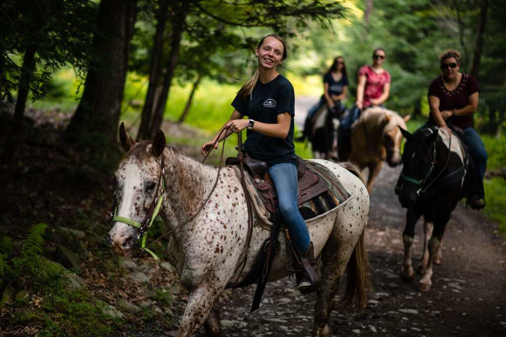 woman in jeans and navy blue tshirt on white and brown speckled horse in woods