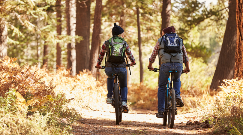 Couple riding bikes on a wooded trail during the fall.